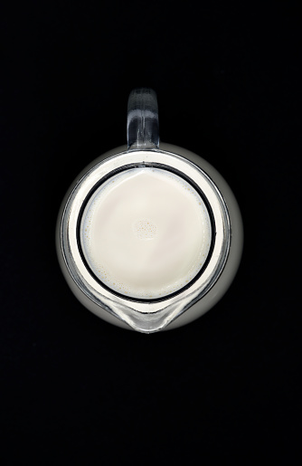 Glass milkman on a black background. A jug of milk. Milk in a vessel.