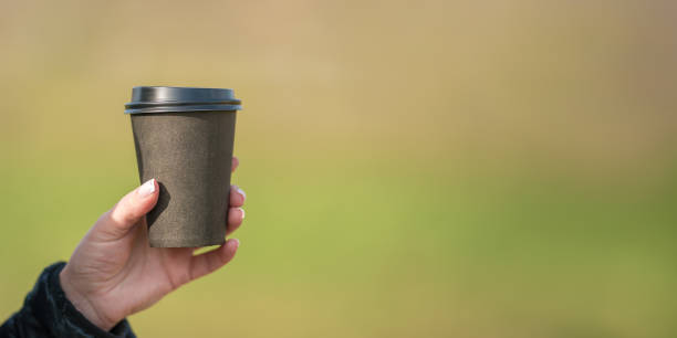 istock Female hand holding paper coffee cup with plastic lid on blurred background 1488913036