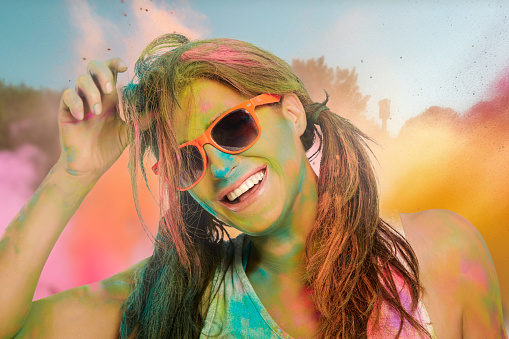 Carefree cheerful woman covered in rainbow colored powder celebrating the festival of colors. Young woman having fun with colorful holi powder outdoors