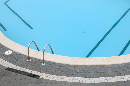 Ladder pool border. Edge pool stair. Swimming pool stone pavement tiles stone paving poolside background blue water surface