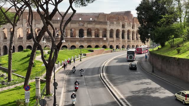 The Colosseum in Rome with tourists on Vespa Piaggio scooters.