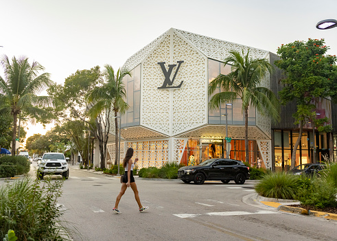 In Miami, USA a woman crosses the street at the intersection in front of the Louis Vuitton store in the Design District neighborhood in the late afternoon.