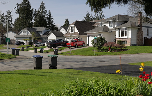 Detached, two-storey houses built in the 1980s stand in a cul-de-sac in Surrey, British Columbia. Recycling and green bins line the Fleetwood neighbourhood on collection day. Spring morning.