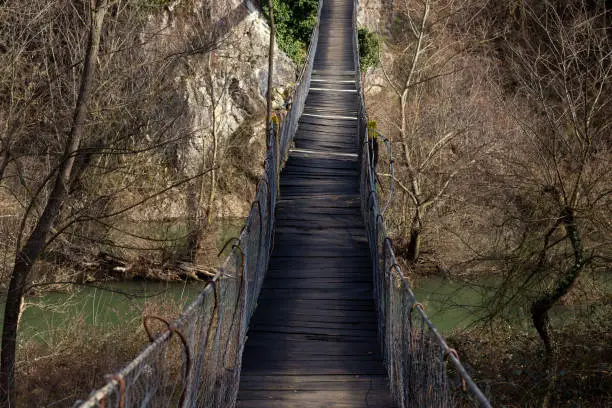 Old wooden bridge hanging over river in nature. Narrow footbridge crossing over forest rocks.