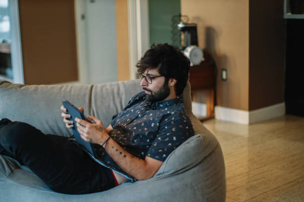 istock man relaxing at home, reading on a digital tablet 1488918478