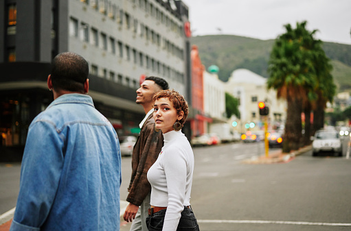Stylish young woman crossing a city street while walking with two male friends in the city