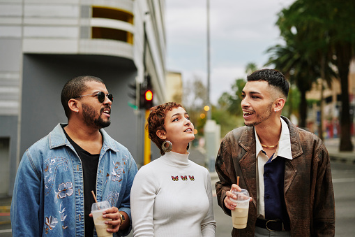 Smiling group of young friends talking and drinking coffee while standing together outside in the city