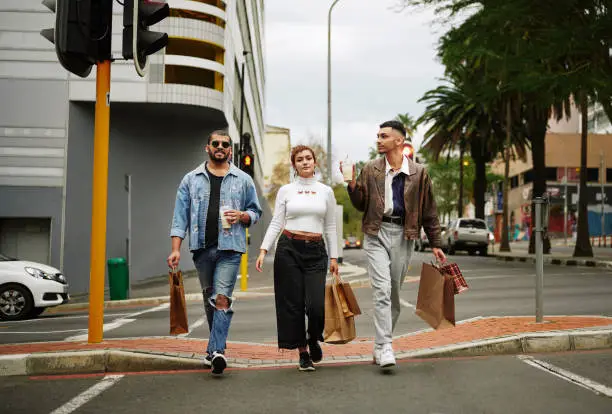 Portrait of a stylish group of young friends with shopping bags drinking coffee while walking together in the city