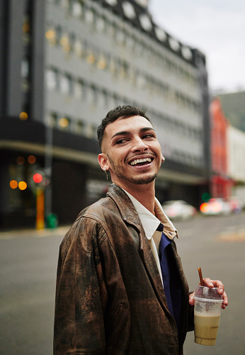 Stylish young man laughing and drinking coffee while walking outside on a city street