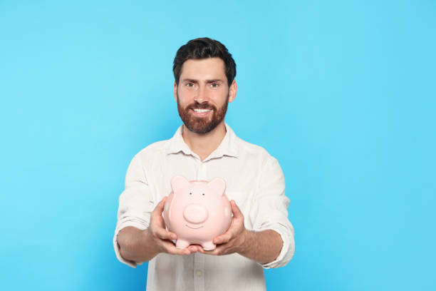 istock Happy man with ceramic piggy bank on light blue background 1488926614
