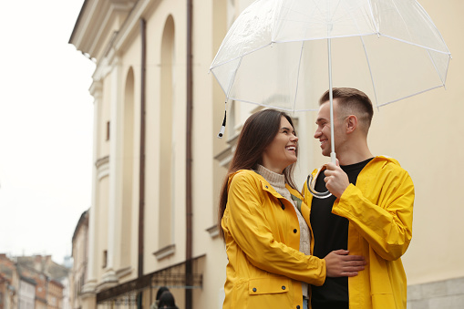 Lovely young couple with umbrella walking under rain on city street