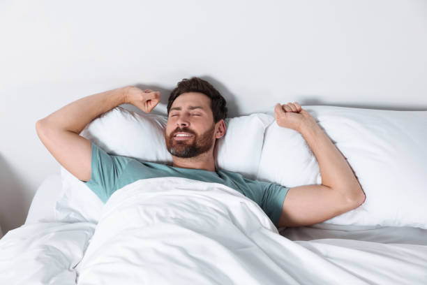 istock Happy man stretching on comfortable pillows in bed at home 1488926981