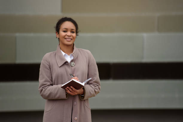 afroamerikanerin in geschäftskleidung mit notizblock führt ein interview vor dem hintergrund eines stadtbildes. - eadership stock-fotos und bilder