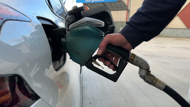 A man holds green fuel nozzle into the gas tank of a car at the gas station