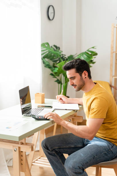 istock Man sitting at desk at home doing bills with calculator. 1488933175