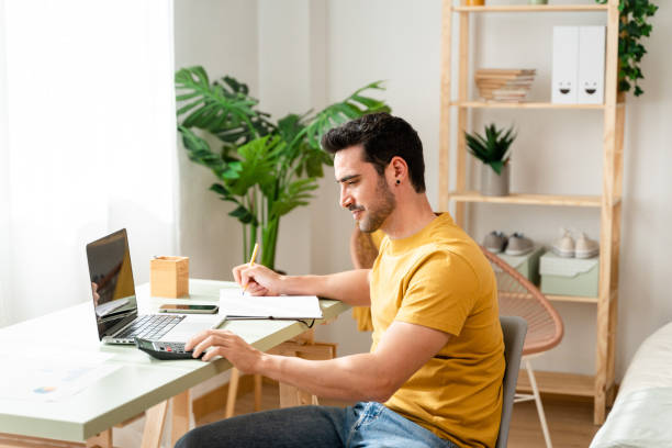 istock Man sitting at desk at home doing bills with calculator. 1488933973