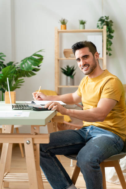 istock Man sitting at desk at home doing bills with calculator. 1488934097