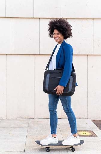 Vertical portrait of a cool african businesswoman in skateboard carrying a bag