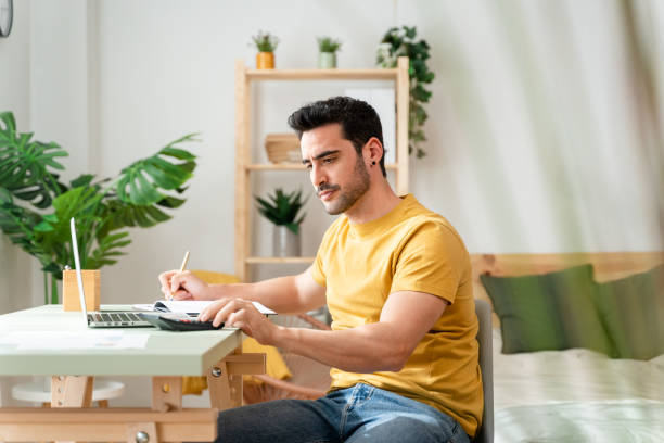 istock Man sitting at desk at home doing bills with calculator. 1488934458