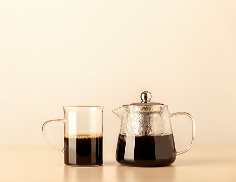 A glass coffee cup and a glass coffee pot with steam in it on a table