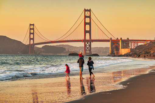 Family enjoys Marshall's Beach with the landmark Golden Gate Bridge in the background in San Francisco California USA during sunset.