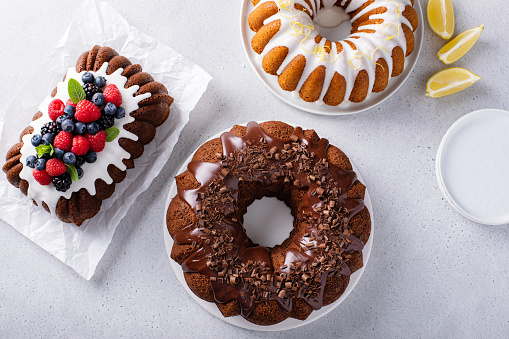 Variety of bundt cakes on the table with lemon, chocolate and berry cakes overhead