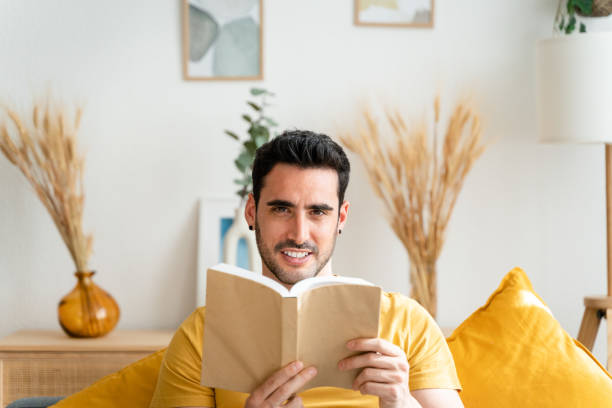 istock Young man at home sitting in a sofa and reading a book. 1488947573