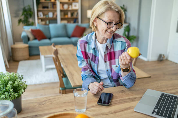 istock Senior woman sits at the kitchen island eats an apple and works at the computer 1488948491