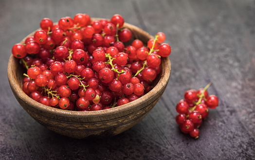 Red ripe currant berries in wooden bowl on a rustic background
