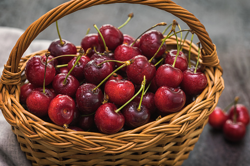 Fresh sweet cherries with water drops in a basket on a rustic background