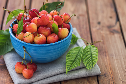 Fresh sweet cherries with water drops in a bowl on a wooden background