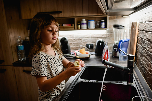 little girl in a kitchen washing fruit.