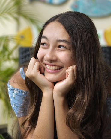 A young Hawaiian teen adolescent girl in her home,  wearing clear transparent dental braces.