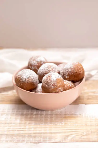 Photo of Paczki Or Zeppole In Pink Bowl With Powdered Sugar On Wooden Table. Fat Thursday Carnival or Tlusty Czwartek, Christian tradition Of Eating Doughnut, Delicious Donuts. Vertical Plane.
