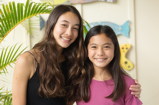 Portrait of two young Hawaiian teen adolescent girls in her home, looking at camera, smiling.