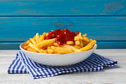 Bowl of tasty french fries on white wooden table