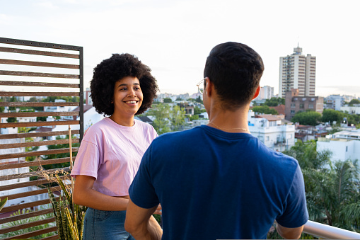 Two young people on the balcony smiling talking and enjoying the view . Wearing pink and Blue shirts and glasses. High quality photo