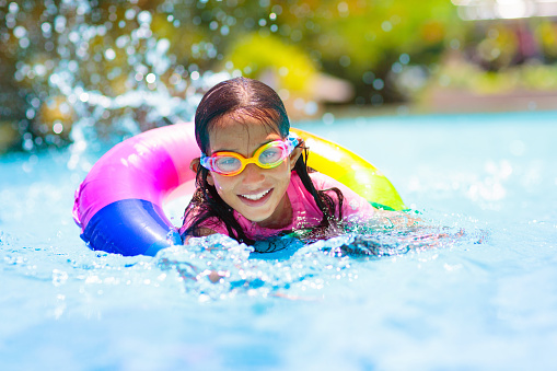 Child in swimming pool floating on toy ring. Kids swim. Colorful rainbow float for young kids. Little boy having fun on family summer vacation in tropical resort. Beach and water toys. Sun protection.