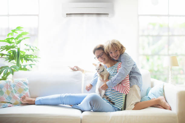 Mother and child with air conditioner remote Mother and child with air conditioner remote control. Comfortable temperature at family home. Cooling and heating device. Mom and kid on couch under cold breeze. Air conditioning on hot summer day. air conditioner family stock pictures, royalty-free photos & images