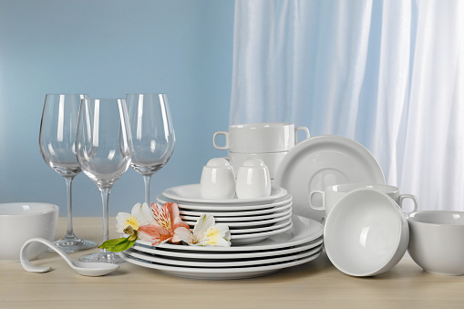 Glasses and clean dishware with flowers on light grey table