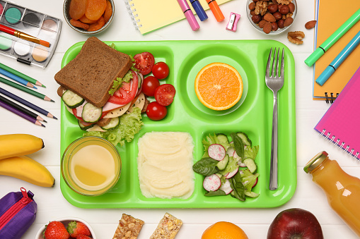 Serving tray of healthy food and stationery on white wooden table, flat lay. School lunch