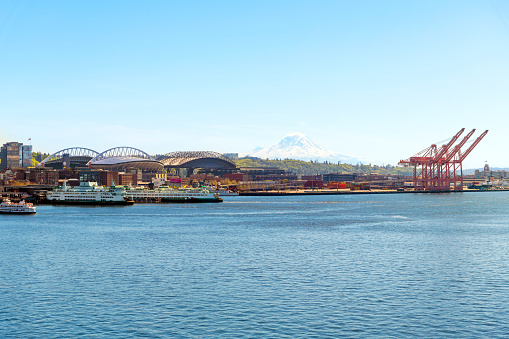 Lumen Field and T-Mobile Park are visible along the waterfront harbor on Puget Sound, with ships lining the Elliott Bay and Mount Rainier in the distance in Seattle, Washington USA.