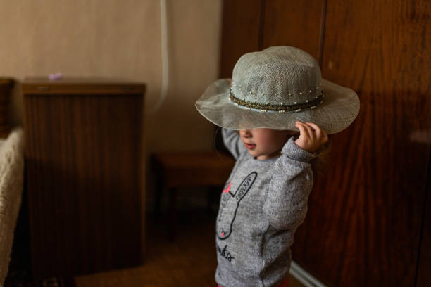 Cute, cheeky 20 month old toddler wearing a sun hat enjoying a walk in the park on a sunny late summers day holding hands with her mum, smiling happily.