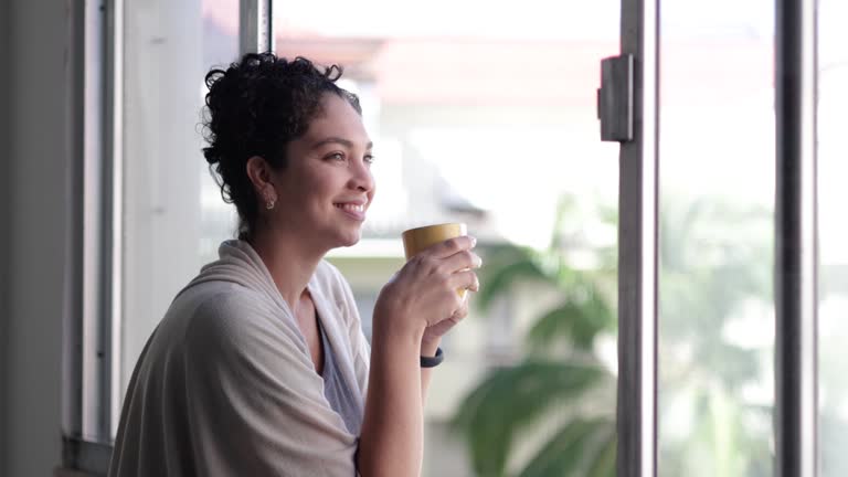 Latin woman having a coffee in the window of her house during a break at work