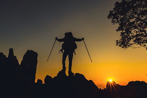 The Man on the mountain. Leadership Concept. Silhouette of hiking man celebrating raising arms on the top of mountain with over sunset or sunrise. Success man on the peak of high rocks