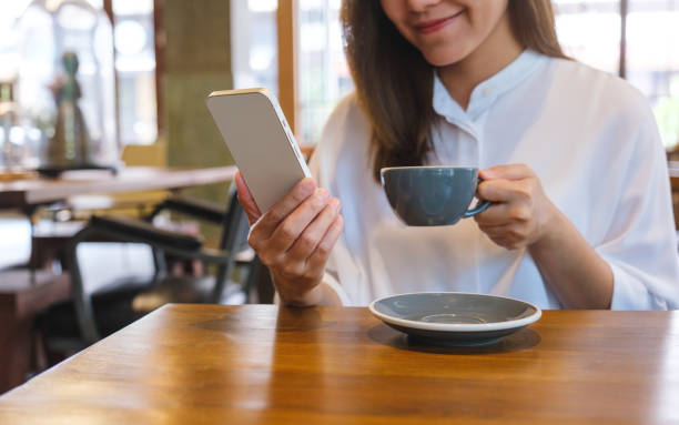 istock Closeup image of a young woman holding and using mobile phone while drinking coffee in cafe 1489017833