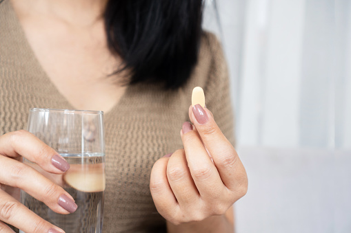 close-up of a woman's hand taking vitamin C supplement with a glass of Water