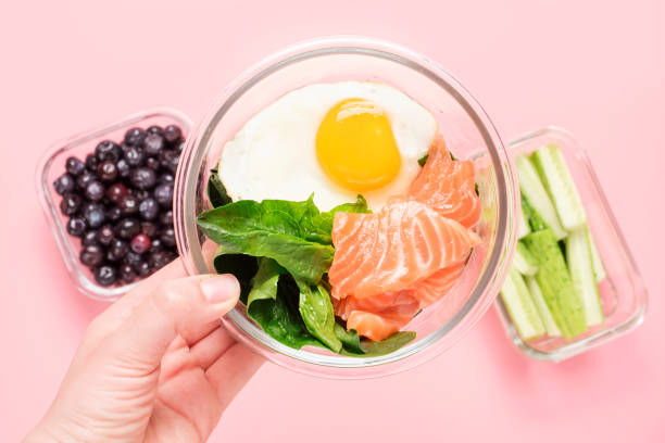 Female hand holding glass lunch box with healthy food on a pink background. stock photo