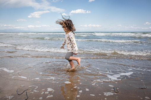 side view of little girl with blown hair dancing and playing with waves at the sea
