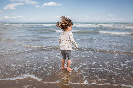 rear view of little girl with blown hair playing with waves at the sea